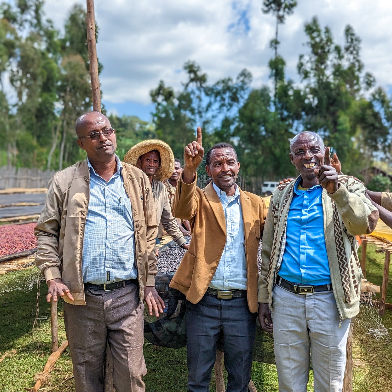 Group of people standing outdoors with a coffee drying rack in the background